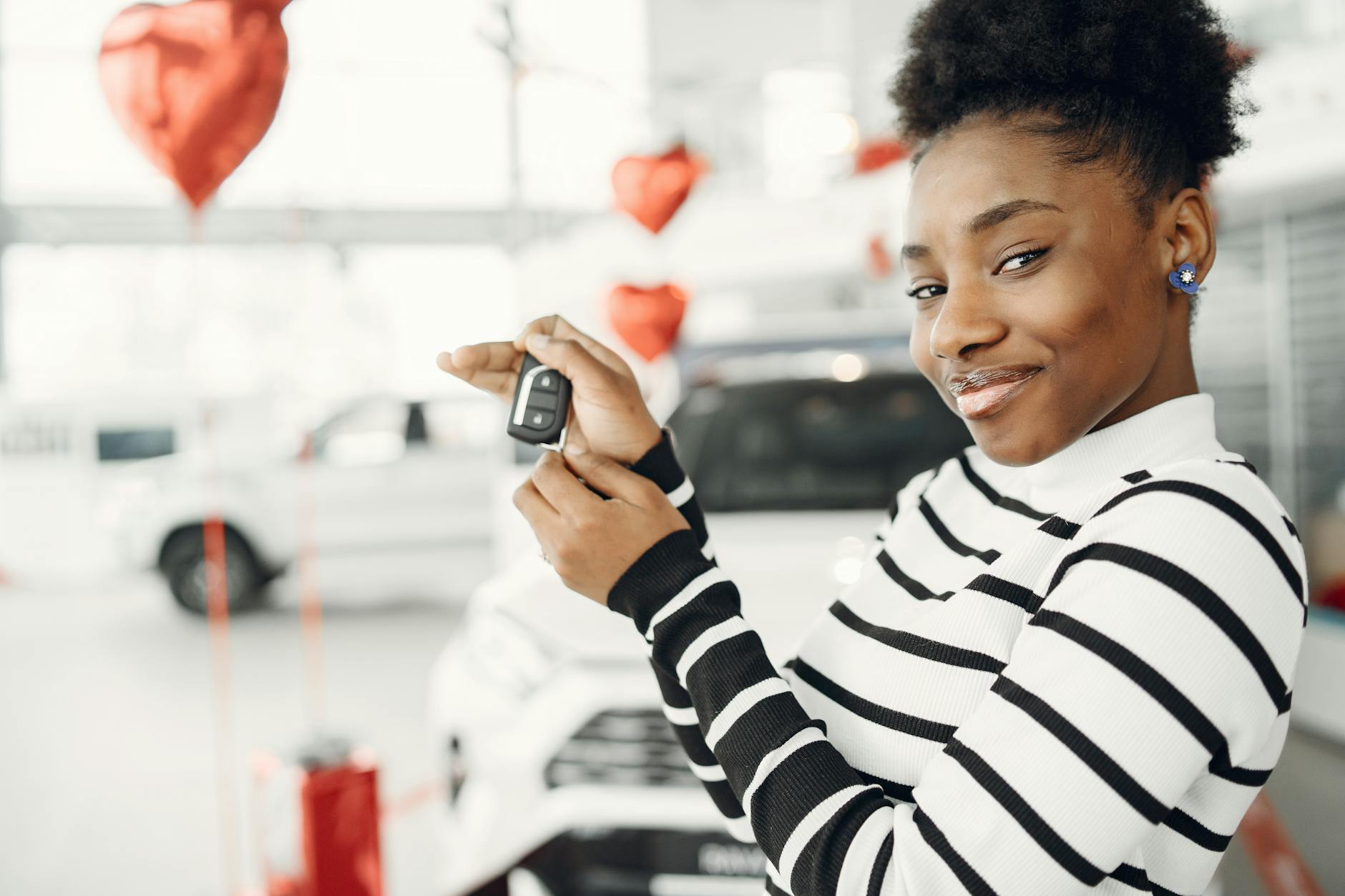 Młoda kobieta trzyma kluczyki do nowego auta w salonie samochodowym